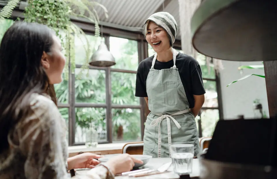 Lachende Servicekraft mit Schürze an einem Tisch im Café